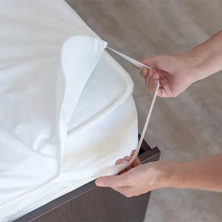 a man putting a strap of a mattress topper to a mattress