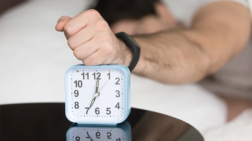 an image of a man oversleeping and turning his alarm clock off