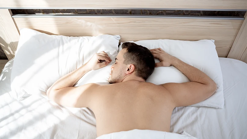 An image of a man sleeping on stomach in his bed.