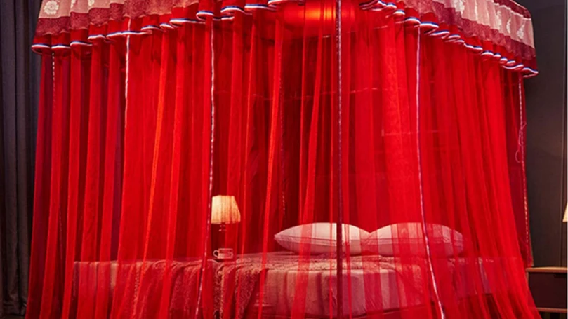 An image of a luxurious four-poster bed with rich red drapes surrounding it