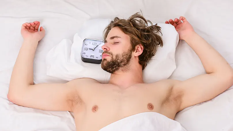 An image of a young man sleeping in hot weather in his bed.