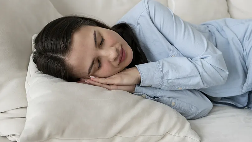 An image of a woman sleeping on a couch with a limited space.