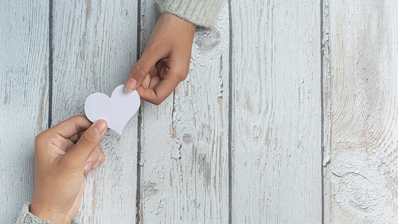 An image of two hands holding a heart on a paper.