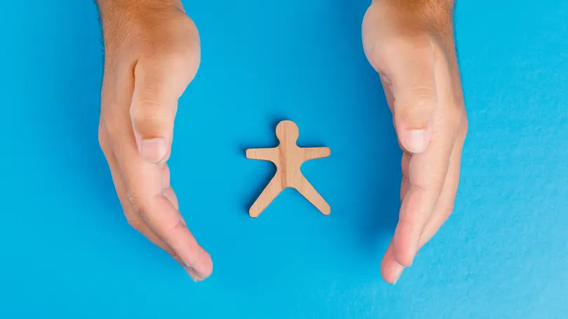 An image of hands shielding a wooden figurine.